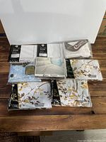 Lot of assorted linens with sheets, pillowcases, and pillow protectors still in packaging laid out on wooden surface.