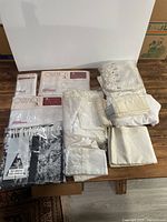 Full assortment of white linens including packaged linens, folded fabrics, and curtains on a wooden surface