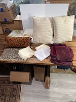 Overview of all linens and pillows laid out on wooden table including two beige pillows, bolster tiger striped pillow, folded linens, and printed fabric pieces