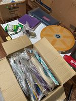 Box open showing various miscellaneous household items including folding paper fans, storage boxes, notebooks, and a circular wooden item.