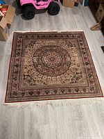 Top-down view of square Persian rug with intricate pattern and fringe on hardwood floor.