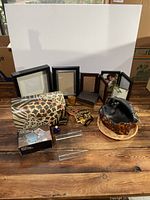 Collection of picture frames, animal print clutch, and decorative items arranged on wood floor.