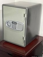 Photo of the small rectangular electronic safe with a digital keypad and LCD screen on the door, showing a gray finish and hinged door.