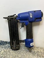 Full view of the blue Campbell Hausfeld pneumatic brad nailer with black handle and magazine.