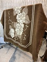 Brown square blanket displayed hanging on rack with cream floral pattern and decorative border.