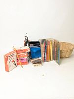 Photo showing various art supplies including boxed oil color paints, colored pencil crayons in plastic case, graphite pencils, and a paint brush wash basin.