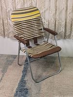 Front view of brown vinyl folding chair with striped fabric seat and backrest on a textured rug, with curtain backdrop.