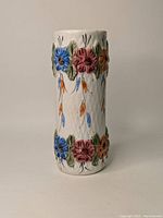 Front and side views of cylindrical ceramic vase with colorful raised flower motifs on white textured base.