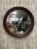 Front view of a circular mirror with dark brown wood frame hung on cream textured fabric background.