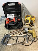 Lot contents including Black & Decker drills in case, saw, dust-covered caulking gun, carpenter's square, and boxes of drill bits.