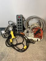 Lot showing Belkin power bar, black extension cord, hanging light with yellow handle, metallic flexible conduit, and coils of electrical wire.