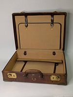 Open vintage brown leather luggage showing tan fabric interior with straps.