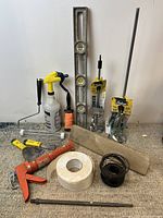 Full lot of mixed paint, plaster, and concrete tools and supplies arranged on carpet including levels, caulking gun, wooden trowel, spray bottle, wiring and rolls.
