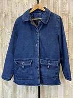 Front view of dark indigo denim jacket hanging against a cream curtain backdrop