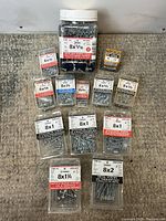 Photo showing assorted 8 size screws in clear boxes and a large jar, including wood screws, particle board screws, and metal screws.