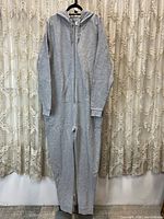Full view of grey fleece onesie hanging on a hanger showing front zipper and hood.