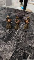 Set of three copper angel figurines standing on a dark marble surface, showing size and grouping.