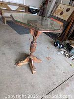 Wooden octagonal end table with glass top and carved pedestal base in garage setting