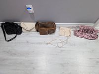 Five assorted vintage purses lined up against a grey wall on light wood flooring, showing variety in color and style.