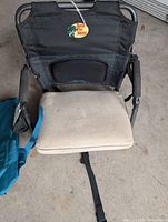 Black foldable outdoor seat with down beige cushion and mesh backrest, Bass Pro Shops tag visible, frame and armrests included