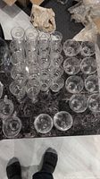 Top-down photo of 30 assorted clear glassware pieces arranged on a dark countertop showing various sizes and types of glasses and cups