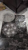 Three clear glass cake stands displayed on a dark marble surface, showing different patterns and pedestal bases.