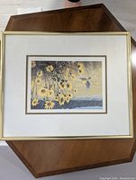 Framed print showing yellow flowers and blue bird motif, neutral matting and gold-tone frame