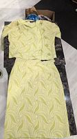 Top-down photo of vintage lime green swirling patterned jacket and matching pencil skirt laid flat on a dark surface