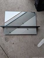Top view of rectangular mirror showing reflective surface and black floating shelf mounted in the middle horizontally.