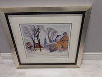 Framed print of "Winter Morning in Baie-Saint-Paul" showing a winter scene with buildings and church steeple under leafless trees, matted and framed in cream colored frame.
