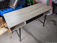 Front angle view of office desk showing light wood surface and open cubby shelving beneath, supported by black metal legs.