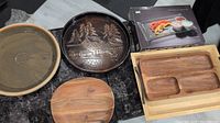 Top-down view of assorted serving dishes including ceramic and wooden trays and the unopened packaged serving set.