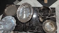 Photo showing multiple metal trays including an oval divided tray, plain round tray, round dish with ladle, and decorative perforated bowl.