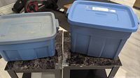 Two blue plastic storage totes placed on tables, different sizes with lids on top.