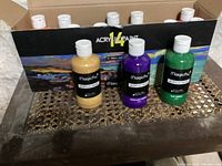 Box containing 14 bottles of 8 oz Magicfly acrylic craft paint, including yellow, purple, green, and others, with some bottles unused and some used.