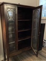 View of antique wooden china cabinet with the left glass door open, showing four interior shelves and wood grain finish.