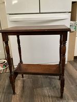 Front view of antique wooden occasional table showing rectangular top, turned legs, and lower shelf book rack.