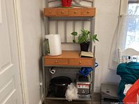 Photo showing bakers rack with wood drawers on metal frame, black slow cooker, food processor, some household items