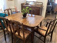 Antique wooden dining table with five chairs, two with armrests, around it; plant on table; visible table leaves
