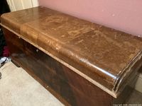 Side angled view of vintage cedar chest showing worn top surface with scratches and wood grain finish.