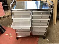 Front view of craft cart showing two columns of five plastic drawers each, metal frame and metal top surface, caster wheels at bottom.