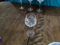 Four crystal hock wine glasses with pinwheel pattern on the bowl, clear stems and bases, arranged on wooden table with shadows visible.