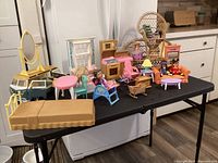 Wide shot of all dollhouse furniture pieces and dolls on a black table surface with kitchen counters in background.