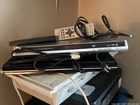 Two DVD players stacked, Toshiba black unit on bottom and Panasonic silver unit on top with two remotes and cables.