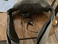 Black Shiatsu 3D rotating neck and shoulder massager with plug and cord shown on wooden table.