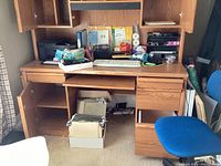 Front view of wooden office desk with various items on the surface and inside shelves, showing overall structure with keyboard tray and file drawer visible.
