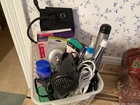 Photo of personal care basket showing curling irons, hair dryer, various bottles, and a box of pantiliners