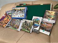 Wooden puzzle board with green felt surface displayed with an assortment of puzzle boxes including Winter skating, tropical island, dinosaur, Halloween pumpkins, classic paintings, and interior scenes.