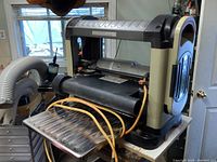 Front-left angle of the Ridgid planer on its stand, showing overall machine condition, infeed table and attached dust collection hose.