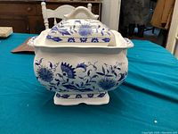 Front view of the blue and white ceramic electric soup tureen with floral patterns on a turquoise surface.